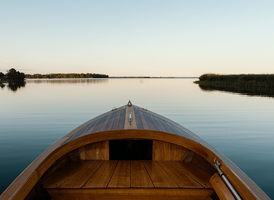 Vy från en träeka som skrider fram på vattnet en vacker och klar sommarkväll.
